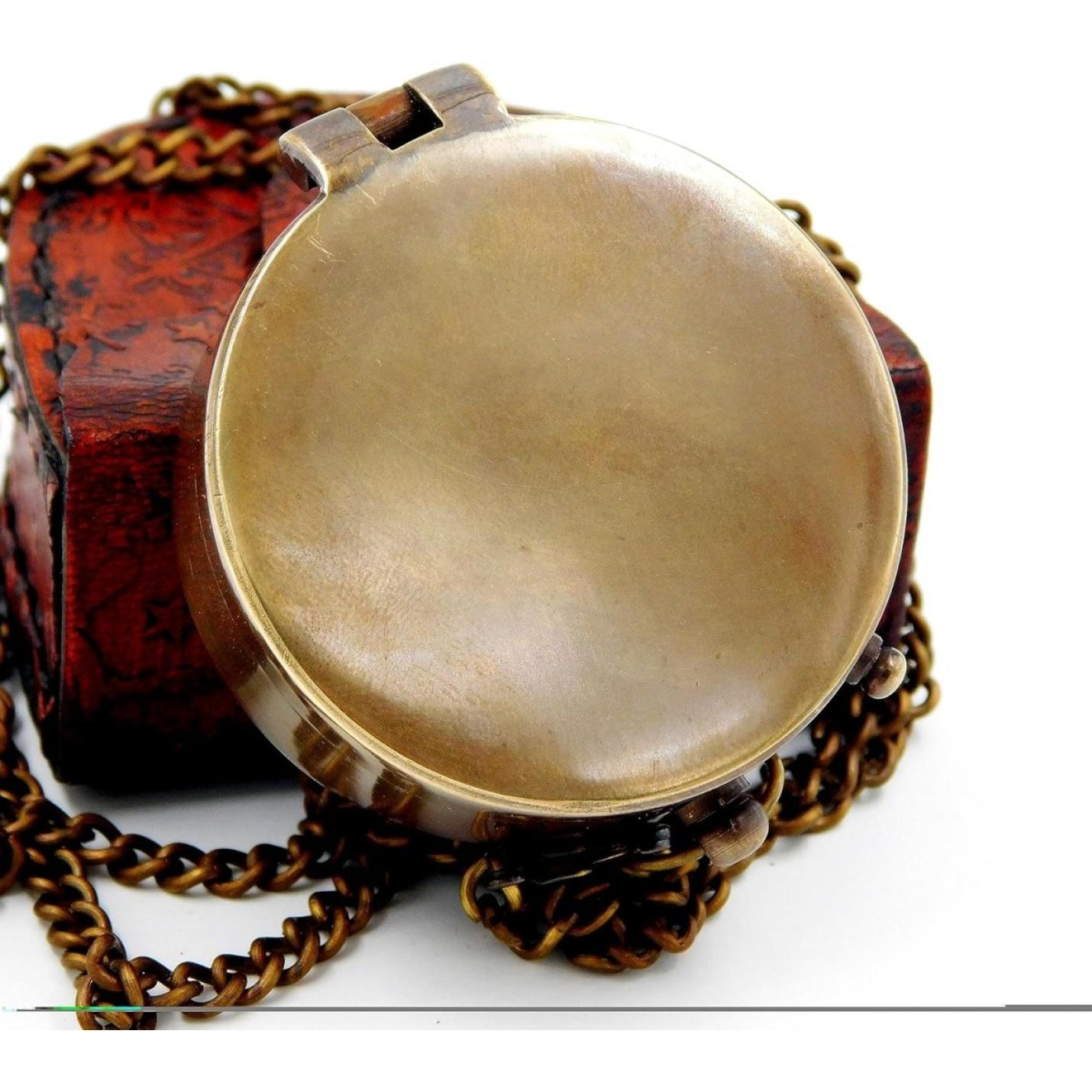 Antiek koperen medaillon aan een ketting, tentoongesteld naast een klein versierd houten doosje met een Handgemaakt messing zakkompas: een klassieke must-have voor outdoorliefhebbers.