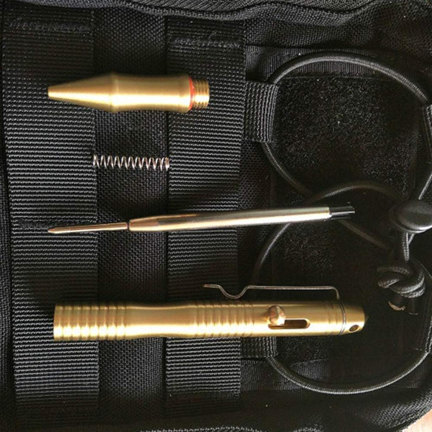 Een tactische Duurzaam massieve messing pen en accessoires geplaatst op een geweven zwarte stoffen ondergrond.