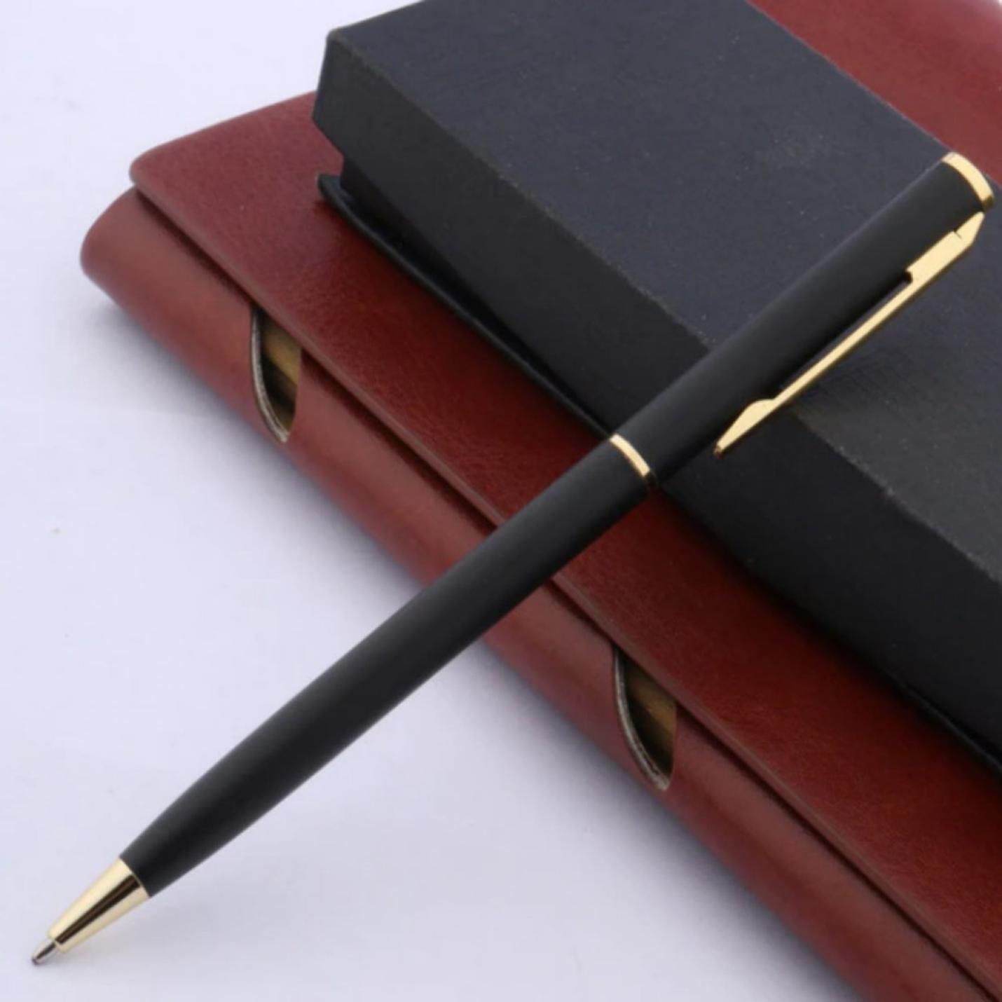 Zin met productnaam: Een betaalbare Ontdek de tijdloze elegantie van klassieke balpennen met gouden accenten rustend op een gesloten bordeauxrood dagboek.