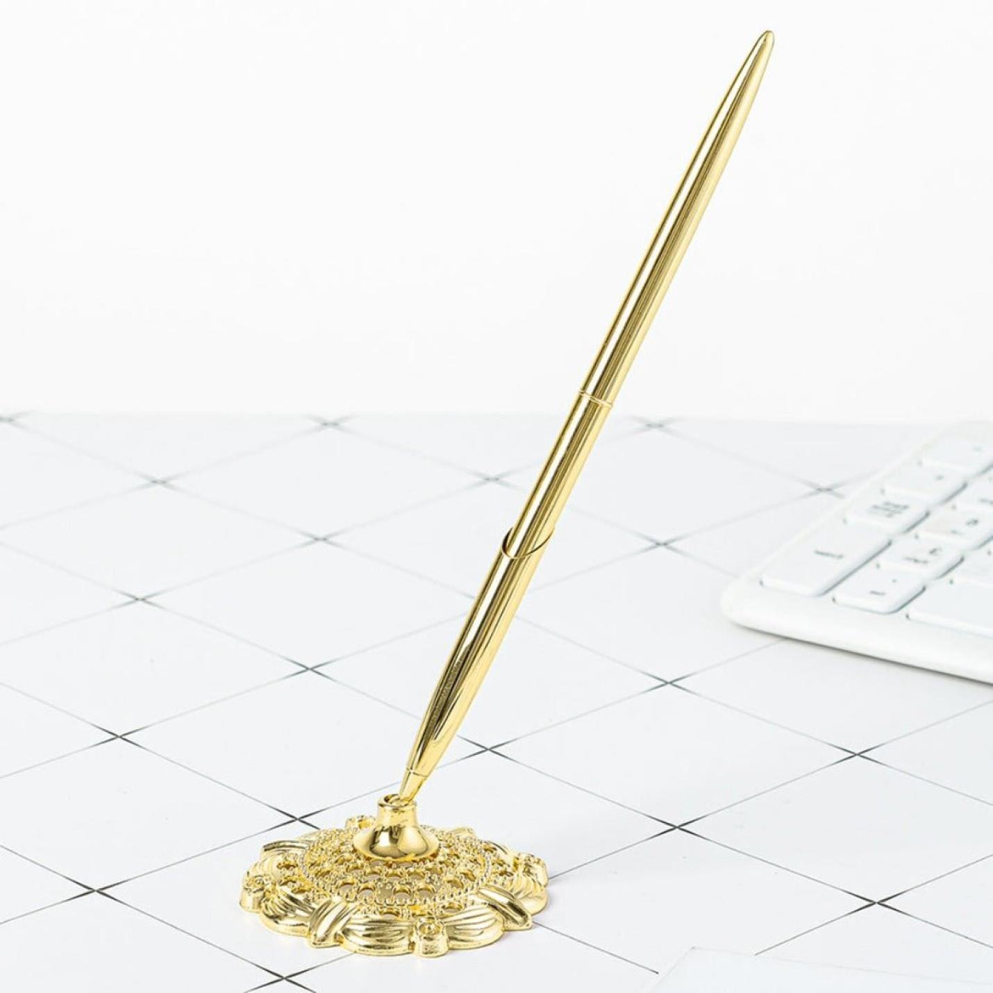 Schrijf met stijl en professionaliteit met deze elegante Schrijf met stijl en professionaliteit met deze elegante gouden zakelijke metalen balpen rustend op een sierlijke houder, geplaatst op een wit bureaurooster met een toetsenbord ernaast.
