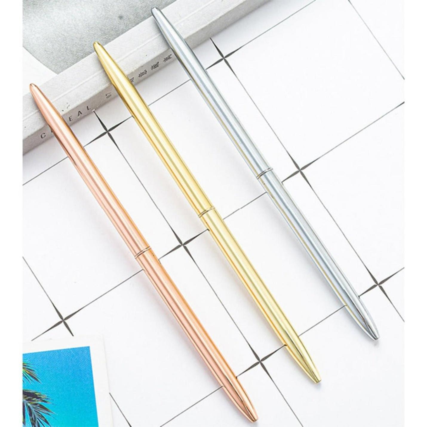 Drie elegante zakelijke metalen balpennen in roze goud, goud en zilveren kleuren, georganiseerd diagonaal over een planner met een rasterontwerp.