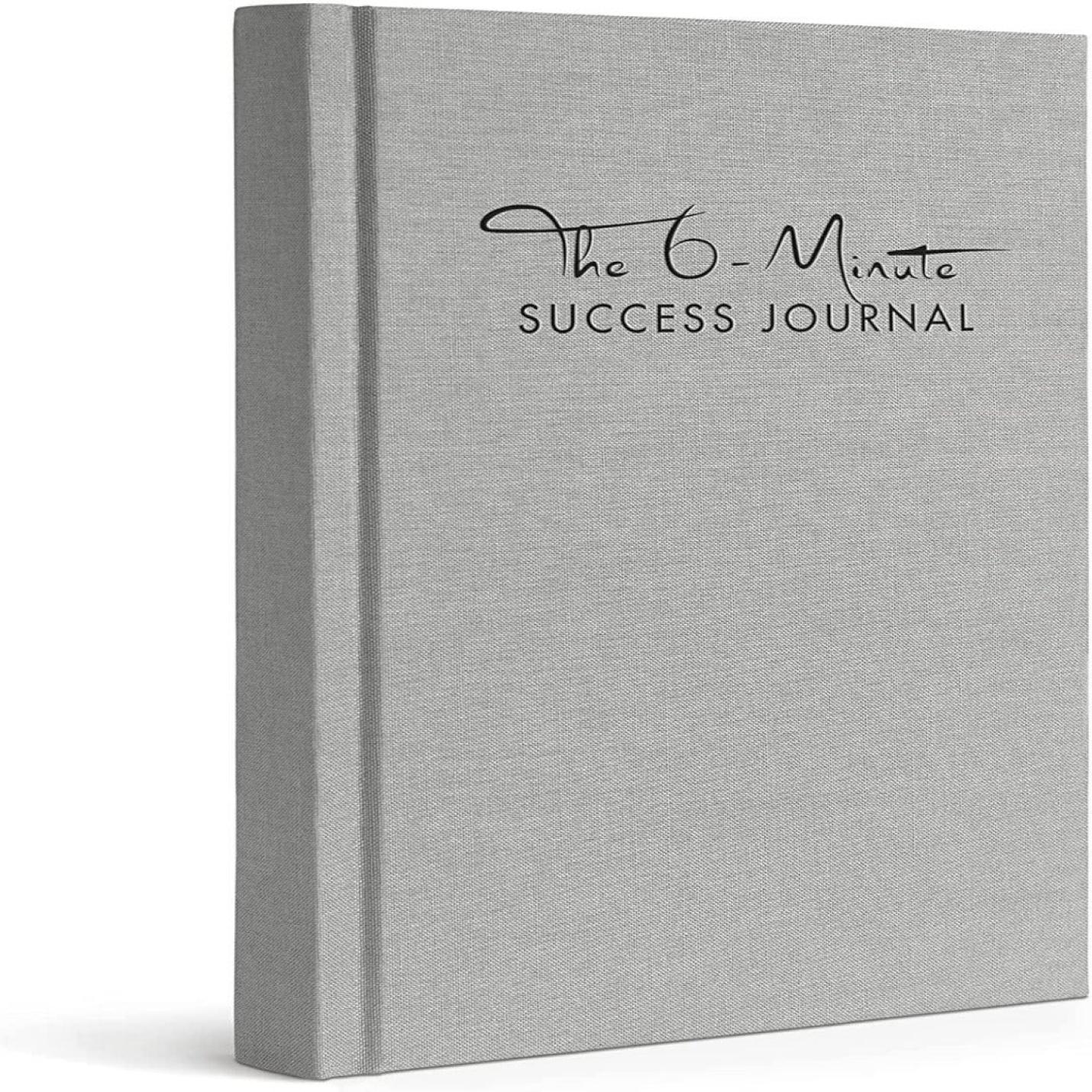 Een grijs hardcover boek met de titel "Het 6-Minute Success Journal: Transformeer je Leven met Slechts 6 Minuten Per Dag!" rechtopstaand weergegeven met een gestructureerde omslag, ontworpen om de productiviteit te verhogen.