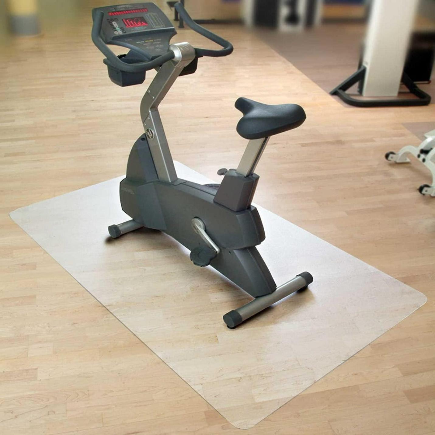 Een hometrainer geplaatst op een Beschermmat voor sporttoestellen in een kamer met houten vloer, met een digitaal display en een verstelbare stoel.