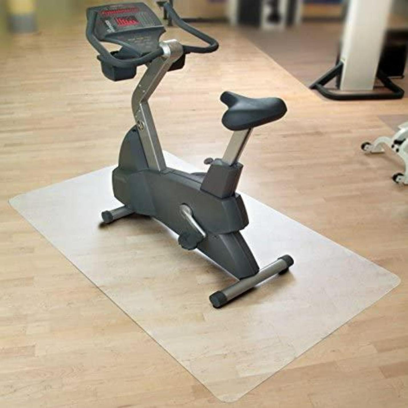 Een hometrainer geplaatst op een Beschermmat voor sporttoestellen op een houten vloer in een kamer met zachte verlichting.