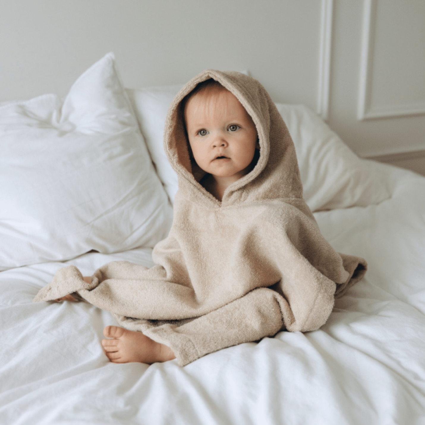 Kindje zittend op bed met Poncho om zich heen