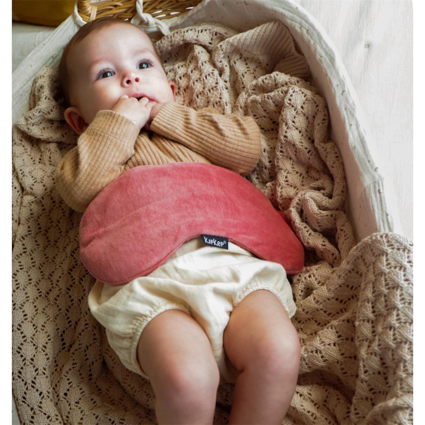 KipKep-woller- Dusty Clay-op buikje baby ligt in een rieten mand
