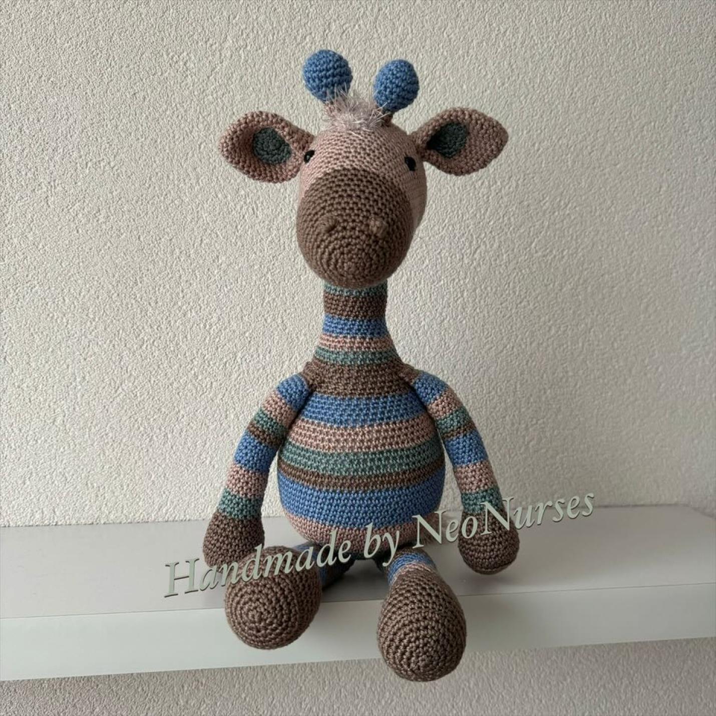 Giraf Gijs Beige is gehaakte zittende giraf beige met blauw en groene strepen en blauwe horens. En bruine voeten, handen en neus